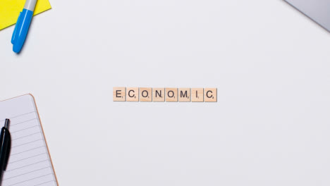 Stop-Motion-Business-Concept-Above-Desk-Wooden-Letter-Tiles-Forming-Word-Economic
