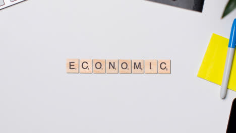 Stop-Motion-Business-Concept-Above-Desk-Wooden-Letter-Tiles-Forming-Word-Economic-1