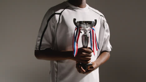 Studio-Portrait-Of-Young-Male-Footballer-Or-Sportsperson-Wearing-Club-Kit-Celebrating-Holding-Trophy-2