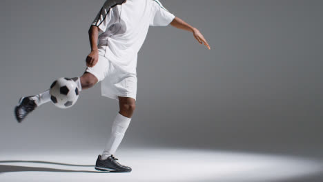 Close-Up-Studio-Shot-Of-Male-Footballer-Wearing-Club-Kit-Controlling-Ball-And-Shooting-At-Goal