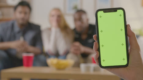 Friends-Celebrating-Watching-Sports-Game-On-TV-At-Home-With-Green-Screen-Mobile-Phone-In-Foreground