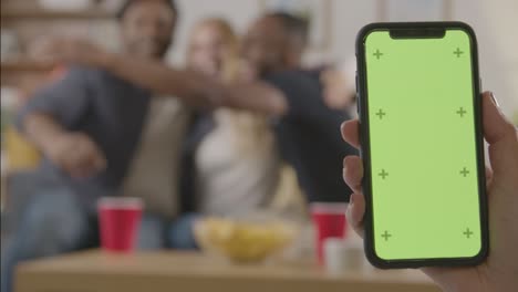 Friends-Celebrating-Watching-Sports-Game-On-TV-At-Home-With-Green-Screen-Mobile-Phone-In-Foreground-1