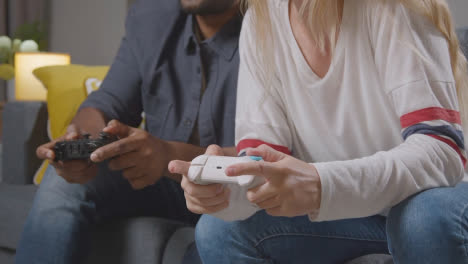 Close-Up-Of-Multi-Cultural-Friends-Or-Couple-Sitting-On-Sofa-At-Home-Gaming-Online-1