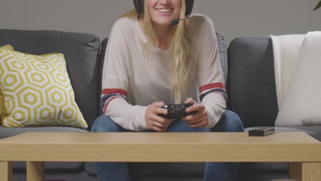Close-Up-Of-Woman-Wearing-Headset-Sitting-On-Sofa-At-Home-Gaming-Online-