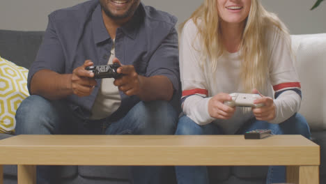Close-Up-Of-Multi-Cultural-Friends-Or-Couple-Sitting-On-Sofa-At-Home-Gaming-Online-