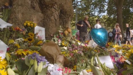 Low-Angle-Shot-of-Floral-Tributes-and-Mourners-In-Green-Park