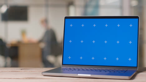 Laptop-Mit-Blauem-Bildschirm-Auf-Dem-Schreibtisch-In-Einem-Geschäftigen-Modernen-Büro