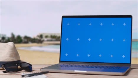 Laptop-Mit-Blauem-Bildschirm-Auf-Dem-Tisch-Mit-Urlaubsstrand-Und-Hotel-Im-Hintergrund