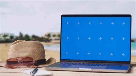 Laptop-Mit-Blauem-Bildschirm-Auf-Dem-Tisch-Mit-Urlaubsstrand-Und-Hotel-Im-Hintergrund