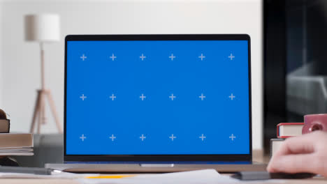 Laptop-Mit-Blauem-Bildschirm-Auf-Dem-Schreibtisch-Zu-Hause,-An-Dem-Der-Student-Arbeitet