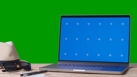 Laptop-Mit-Blauem-Bildschirm-Auf-Dem-Tisch-Mit-Urlaubszubehör-Und-Grünem-Hintergrund