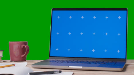 Blue-Screen-Laptop-With-Books-On-Table-With-Green-Screen-Background