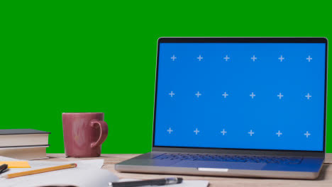 Blue-Screen-Laptop-With-Books-On-Table-With-Green-Screen-Background-1