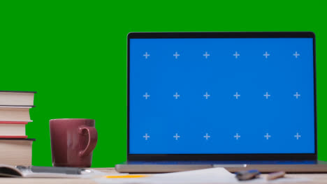 Blue-Screen-Laptop-With-Books-On-Table-With-Green-Screen-Background-2