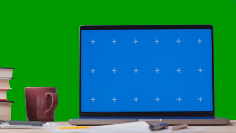 Blue-Screen-Laptop-With-Books-On-Table-With-Green-Screen-Background-3