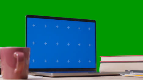 Blue-Screen-Laptop-With-Books-On-Table-With-Green-Screen-Background-Education-Concept-4