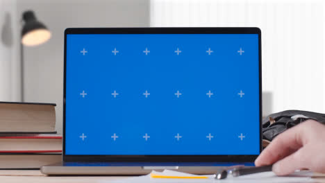 Laptop-Mit-Blauem-Bildschirm-Auf-Dem-Schreibtisch-Zu-Hause,-An-Dem-Der-Student-Arbeitet