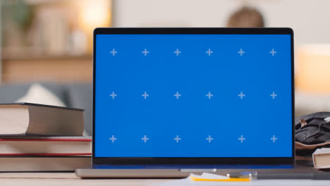 Blue-Screen-Laptop-on-Desk-At-Home-With-Student-Working-In-Background-1