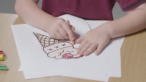 Close-Up-Of-Child-At-Home-Colouring-In-Picture-Of-Ice-Cream-At-Table-