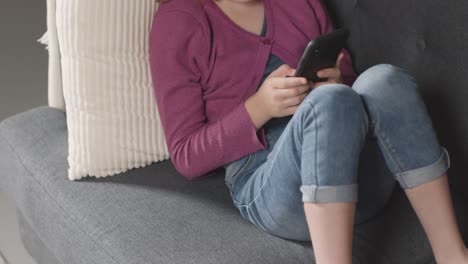 Close-Up-Of-Girl-Sitting-On-Sofa-At-Home-Looking-Online-Using-Mobile-Phone-2