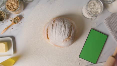 Overhead-Shot-Of-Freshly-Baked-Loaf-Of-Bread-On-Marble-Surface-With-Digital-Tablet