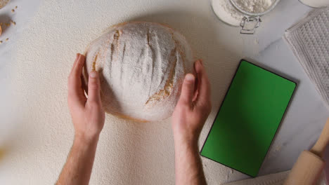 Overhead-Shot-Of-Freshly-Baked-Loaf-Of-Bread-Being-Picked-Up-From-Marble-Surface-With-Digital-Tablet