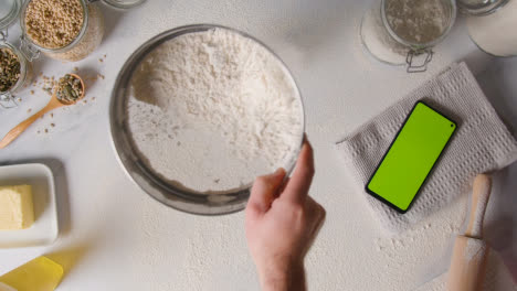 Overhead-Shot-Of-Flour-Being-Sieved-Onto-Work-Surface-For-Baking-With-Green-Screen-Mobile-Phone