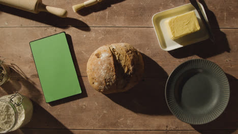 Overhead-Shot-Of-Freshly-Baked-Loaf-Of-Bread-On-Wooden-Table-With-Green-Screen-Digital-Tablet