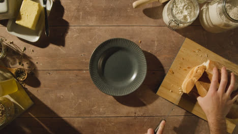 Overhead-Shot-Of-Person-Cutting-And-Buttering-Slice-Of-Fresh-Bread-On-Wooden-Table