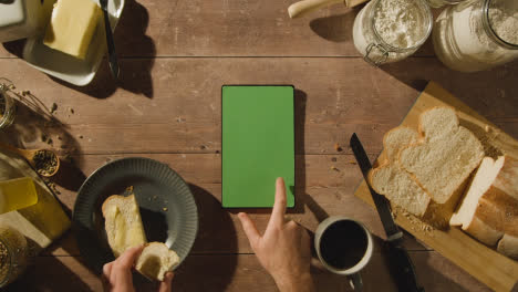 Overhead-Shot-Of-Person-Eating-Freshly-Baked-Bread-With-Butter-On-Wooden-Table-With-Green-Screen-Digital-Tablet-1