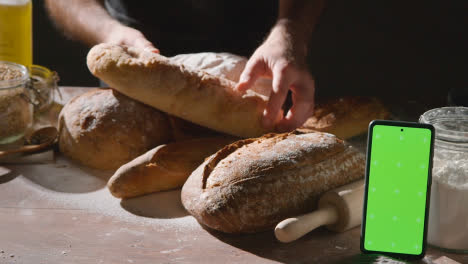 Low-Key-Shot-Of-Freshly-Baked-Loaves-Of-Bread-On-Work-Surface-With-Green-Screen-Mobile-Phone
