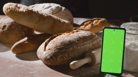 Low-Key-Shot-Of-Freshly-Baked-Loaves-Of-Bread-On-Work-Surface-With-Green-Screen-Mobile-Phone-1