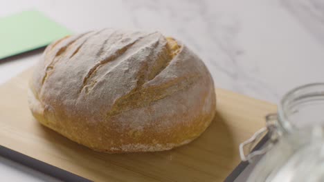 Shot-Of-Freshly-Baked-Loaf-Of-Bread-Being-Picked-Up-From-Marble-Work-Surface