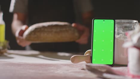 Person-Putting-Freshly-Baked-Loaf-Of-Bread-On-Work-Surface-With-Green-Screen-Mobile-Phone