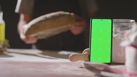 Person-Putting-Freshly-Baked-Loaf-Of-Bread-On-Work-Surface-With-Green-Screen-Mobile-Phone-1