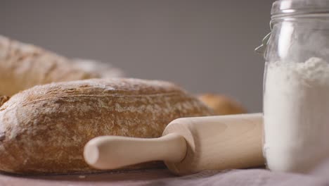 Studio-Shot-Of-Freshly-Baked-Loaves-Of-Bread-On-Floured-Work-Surface-With-Utensils-And-Ingredients