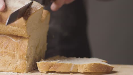 Close-Up-Of-Person-Cutting-Slices-Of-Fresh-Bread-From-Loaf-On-Wooden-Table-1