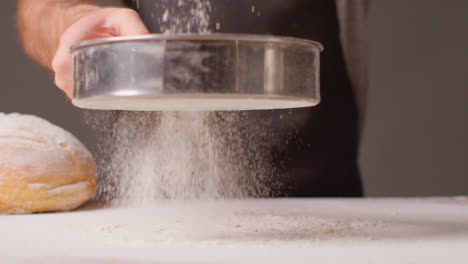 Person-In-Apron-Sieving-Flour-Onto-Work-Surface-For-Baking-With-Loaf