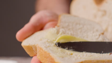 Studio-Close-Up-Of-Person-Buttering-Slice-Of-Fresh-Bread-With-Knife