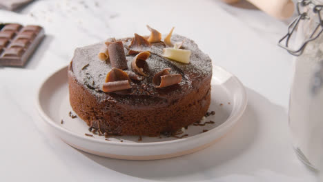 Homemade-Chocolate-Cake-On-Plate-On-Kitchen-Work-Surface-Behind-Ingredients-1