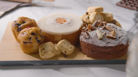 Homemade-Cakes-And-Biscuits-On-Plate-On-Kitchen-Work-Surface-Behind-Ingredients