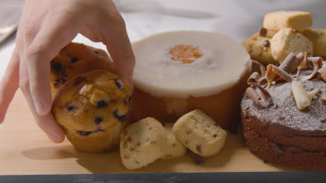 Hand,-Die-Hausgemachtes-Muffin-Mit-Kuchen-Und-Keksen-Auf-Teller-Auf-Küchenarbeitsfläche-Auf-Brett-Legt