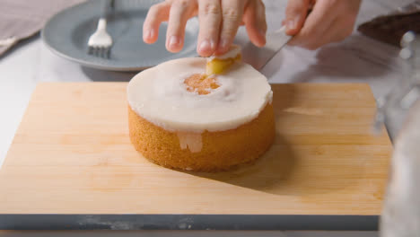 Person-Cutting-Slice-Of-Homemade-Lemon-Drizzle-Cake-Onto-Plate-On-Kitchen-Work-Surface