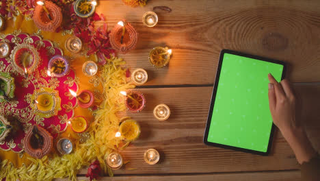 Overhead-Aufnahme-Einer-Person,-Die-Ein-Digitales-Tablet-Mit-Grünem-Bildschirm-Und-Brennenden-Lampen-Verwendet,-Um-Das-Diwali-Fest-Zu-Feiern