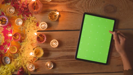 Overhead-Shot-Of-Person-Using-Green-Screen-Digital-Tablet-With-Burning-Lamps-Celebrating-Festival-Of-Diwali-1