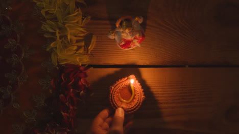 Hand-Putting-Diya-Lamp-On-Table-Decorated-For-Festival-Of-Diwali-With-Statue-Of-Ganesh