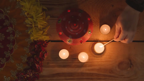 Clay-Pot-With-Tea-Lights-Being-Lit-To-Celebrate-Indian-Wedding-Diwali-Or-Navratri-On-Decorated-Table
