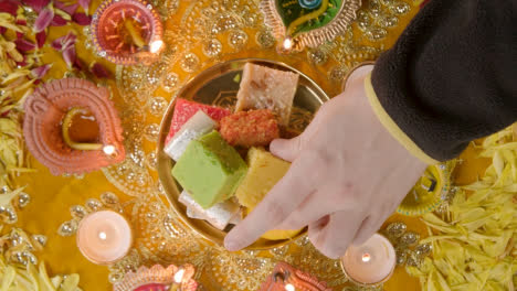 Überkopfaufnahme-Einer-Hand,-Die-Indische-Süßigkeiten-In-Einer-Schüssel-Auf-Einem-Tisch-Aufhebt,-Der-Dekoriert-Ist,-Um-Das-Diwali-Fest-Zu-Feiern