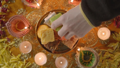 Überkopfaufnahme-Einer-Hand,-Die-Indische-Süßigkeiten-In-Einer-Schüssel-Auf-Einem-Tisch-Aufhebt,-Der-Dekoriert-Ist,-Um-Das-Fest-Von-Diwali-1-Zu-Feiern