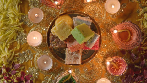 Overhead-Shot-Of-Hands-Picking-Up-Indian-Sweets-In-Bowl-On-Table-Decorated-To-Celebrate-Festival-Of-Diwali